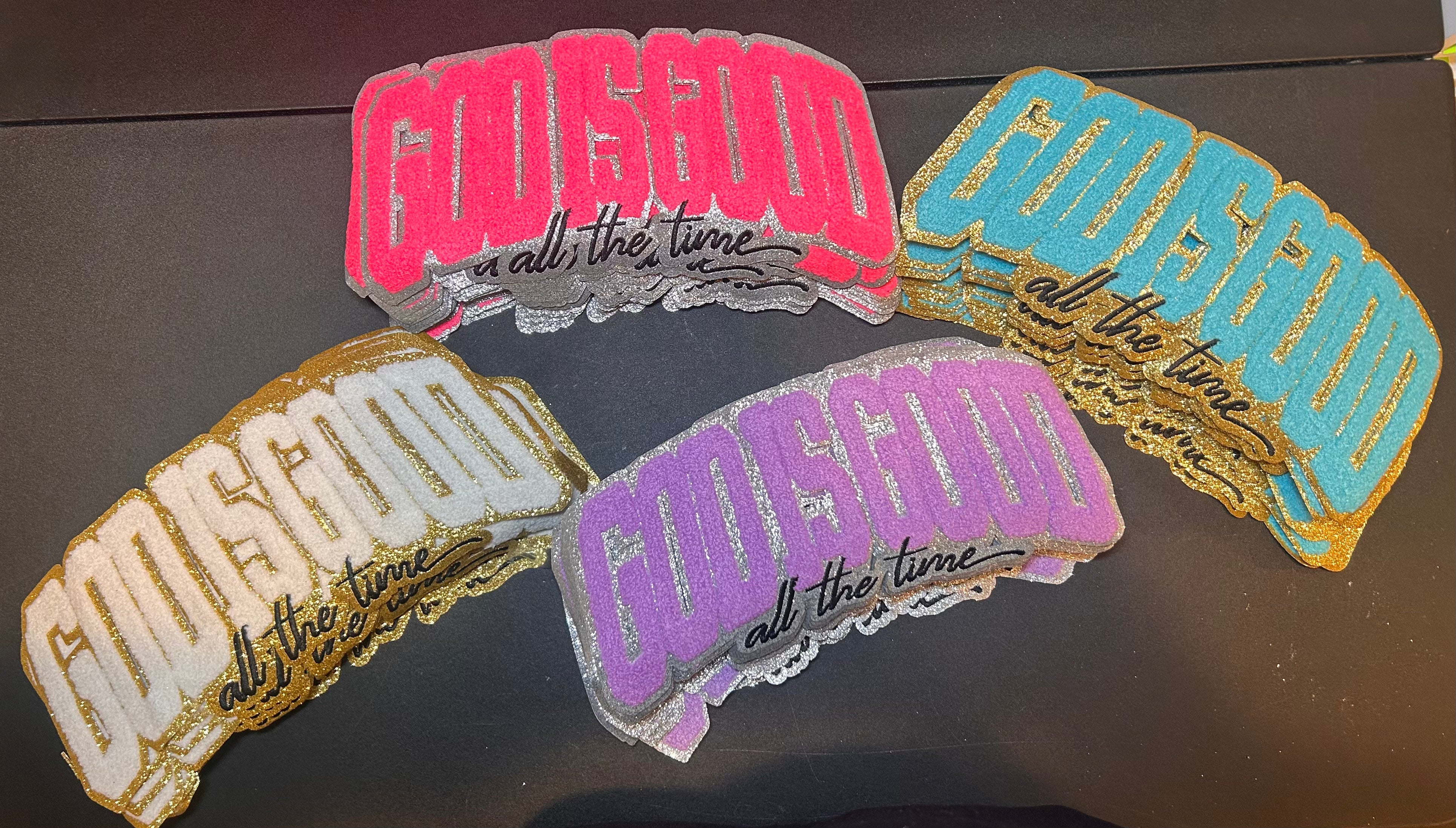 Five colorful 'GOD IS GOOD all the time' patches on a dark surface